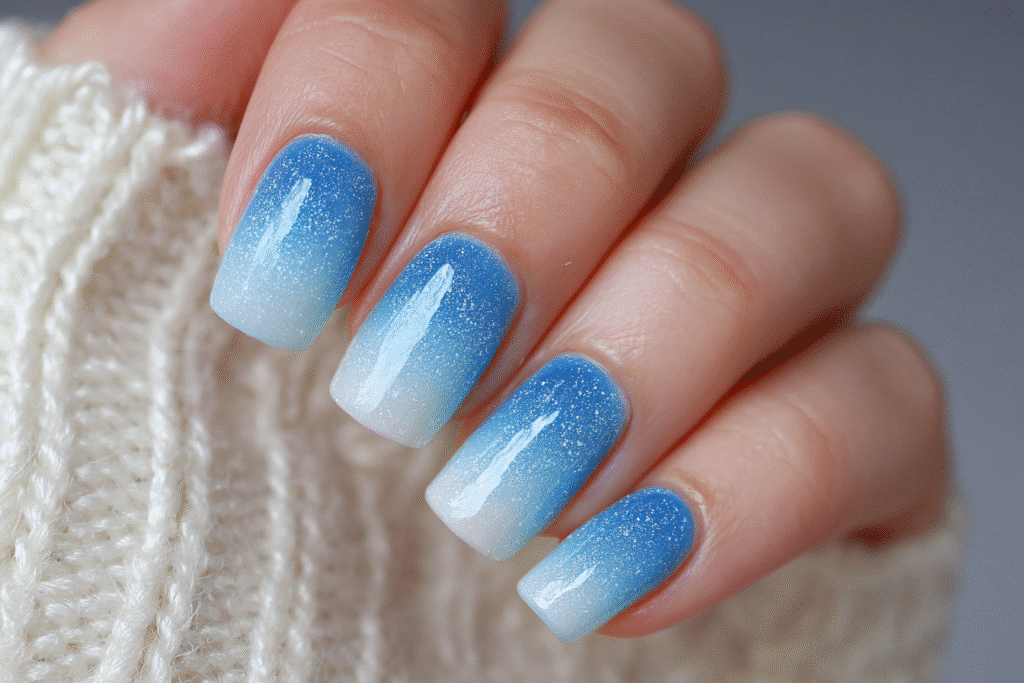 Close-up of summer gel nails with ocean blue ombre fade and glittery glossy finish